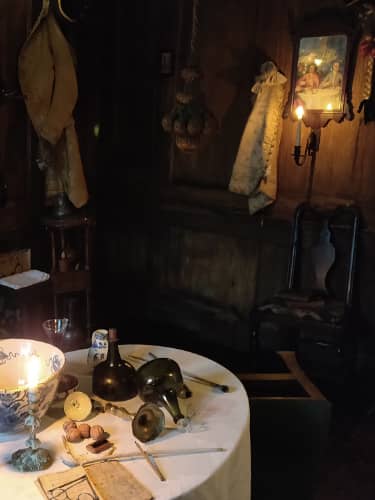 A dark panelled room with candles burning and furniture scattered about.