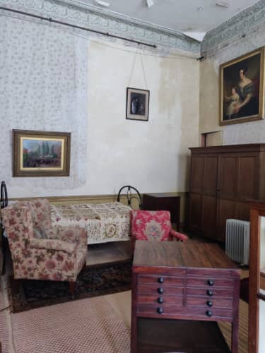 A room with peeling wallpaper and old furniture.